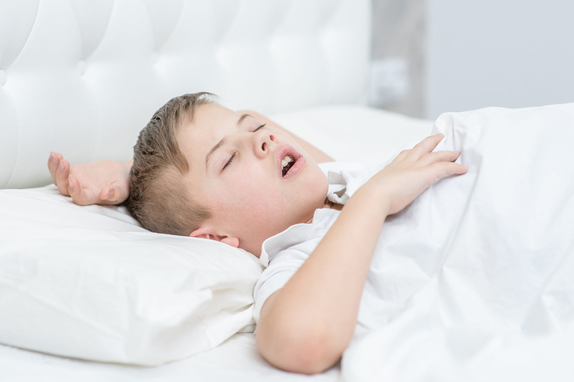 Boy is sleeping on the bed with his mouth open, snoring